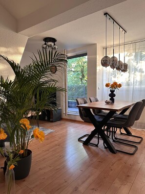 Un espace repas moderne avec une table en bois, des chaises noires et une plante en pot ornée de fleurs jaunes.