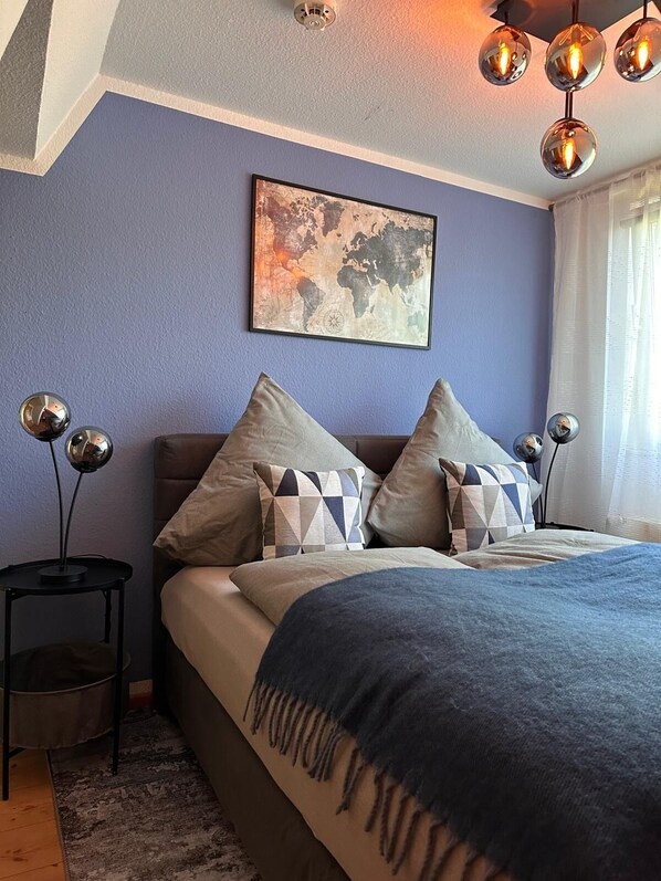 Une chambre à coucher avec un lit, des oreillers, une œuvre d’art représentant une carte du monde, une lampe en forme de globe terrestre et un luminaire au plafond.