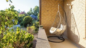 En hængekøje på en balkon med murstensvæg og udsigt til en have.
