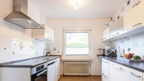 Et moderne køkken med hvide skabe, indbygget ovn, opvaskemaskine og et vindue med naturligt lys.