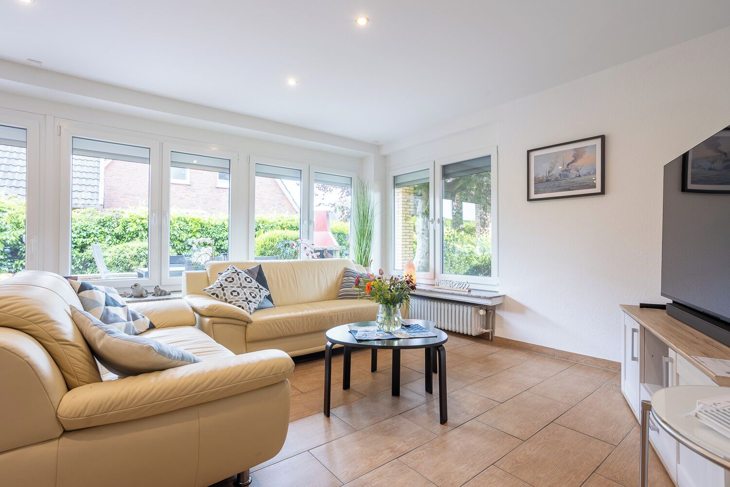 A spacious living room with a beige sofa, a coffee table, and a large window providing a view of greenery outside.