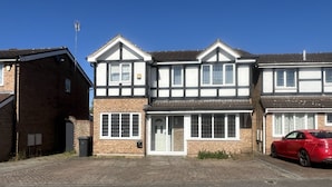 A two-story house with a traditional design, featuring a front door, multiple windows, and a driveway. - Charming Houghton Regis House With 4 Bedrooms (Dunstable)