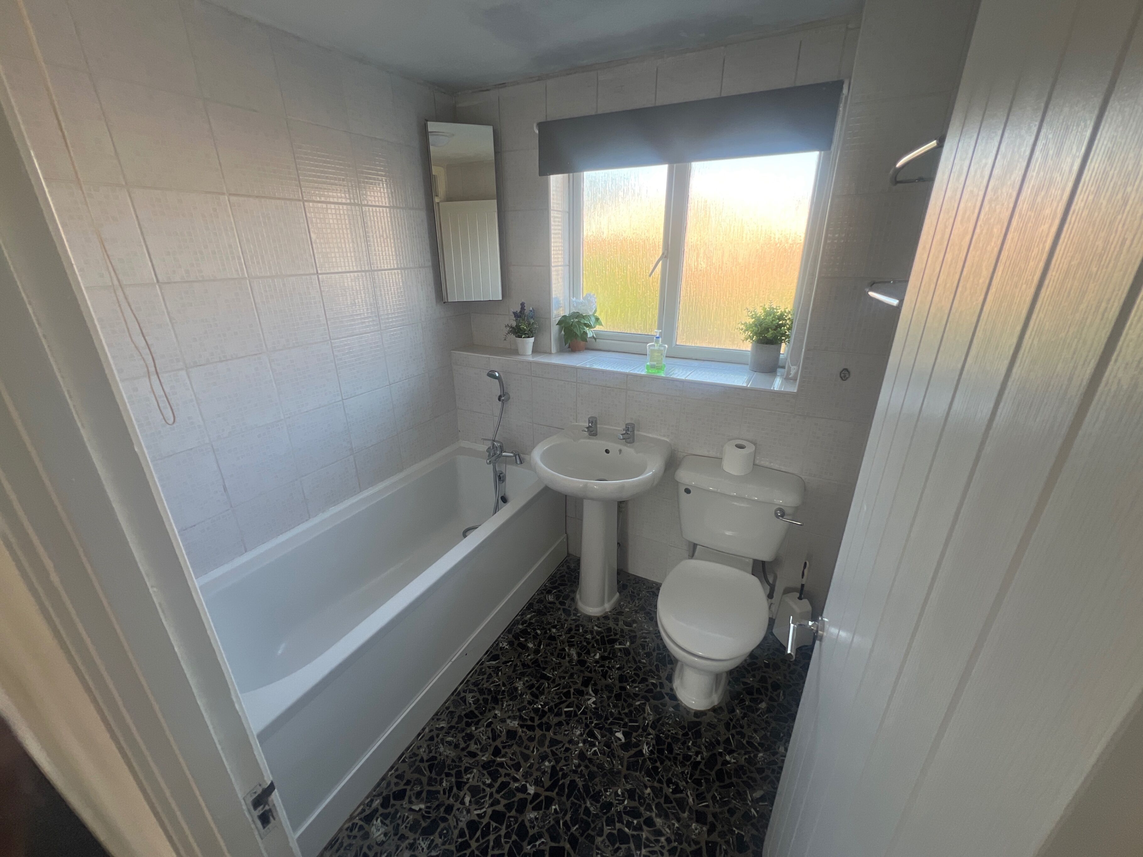 Un baño con bañera, lavamanos, inodoro y una ventana con plantas.
