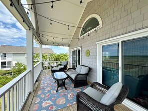 A covered porch with wicker furniture, a patterned rug, and a view of neighboring houses. - Captain's Quarters 6 Bed/4.5 Bath Surf City (Surf City)