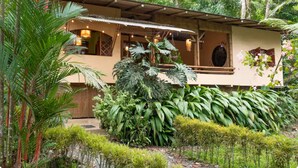 Un bâtiment rustique doté d’un porche abrité, entouré d’une végétation tropicale luxuriante.
