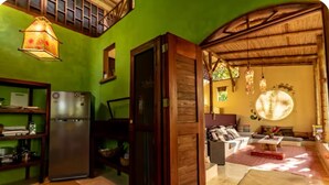 Une pièce avec un mur vert, une porte en bois, un coin cuisine avec un réfrigérateur et un espace salon avec un canapé et une table basse.