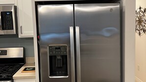 A stainless steel refrigerator with a water dispenser, a microwave, and a stove in a kitchen with white cabinets and a potted plant on top.