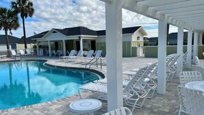 A pool area with lounge chairs and tables, surrounded by buildings with a covered patio.