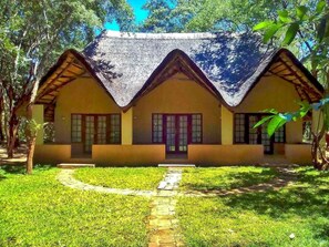 A traditional house with a thatched roof, a central entrance, and a pathway leading to the front door. - Bushfront Lodge (Livingstone)