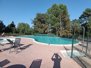A swimming pool with a curved edge, surrounded by a brick patio and green fencing.