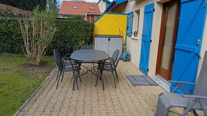 A patio with a round table and chairs, a blue door, and a yellow wall. - House in vacation residence 4 persons swimming pool, tennis, petanque, sneakers (Saint-Julien-en-Born)