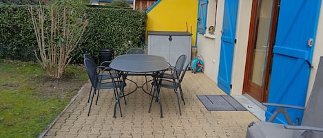 A patio with a round table and chairs, a blue door, and a yellow wall.