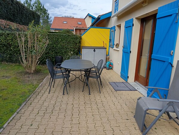 A patio with a round table and chairs, a blue door, and a yellow wall.