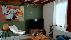 A living room with a TV, a painting, a wicker chair, a sofa, and a wooden coffee table. - House in vacation residence 4 persons swimming pool, tennis, petanque, sneakers (Saint-Julien-en-Born)