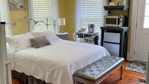 A bedroom with a bed, bedside tables, a bench, a ceiling light fixture, and a microwave on a shelf.