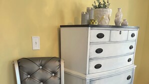 A tufted leather chair with a metal frame, a white dresser with multiple drawers and knobs, and a small potted plant on top.