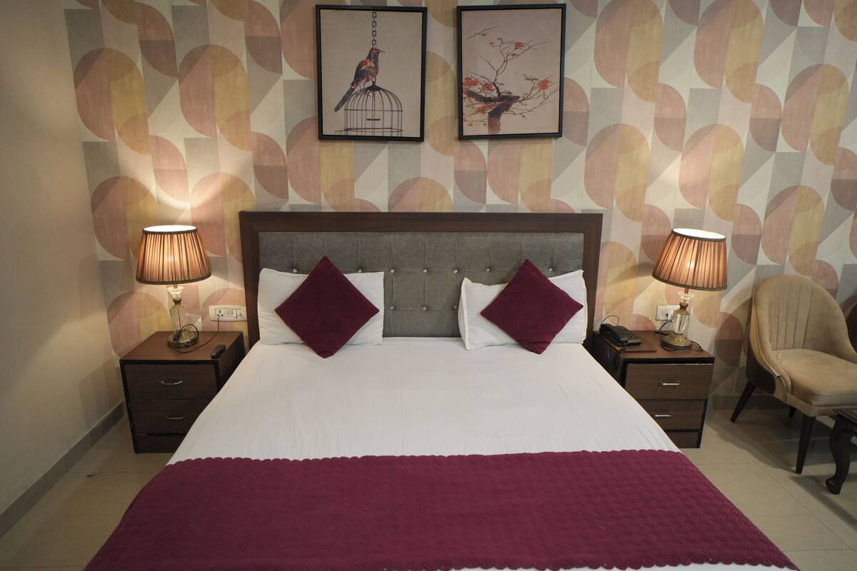 Ein Hotelzimmer mit einem großen Bett, zwei Nachttischen mit Lampen, einem Sessel und zwei gerahmten Bildern an der Wand.