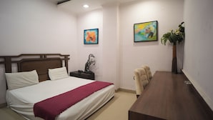 Une chambre d’hôtel avec un lit, un bureau, une chaise, un téléphone et deux tableaux accrochés au mur.
