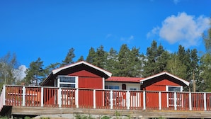 A cabin with a red exterior and white trim, featuring a wooden deck and a white fence.