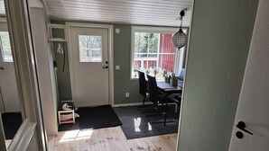 A room with a wooden floor, a door with a small step, a table with chairs, and a window with a view of trees.