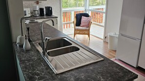 A modern kitchen with a double sink, a microwave, and a coffee maker. There is a wicker chair near a large window.