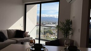 Una sala de estar moderna con un sofá, una mesa de comedor y grandes ventanales que ofrecen vistas de la ciudad.