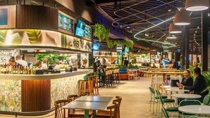Un restaurante moderno con zona de bar, disposición de mesas y un techo con vigas y luminarias a la vista.