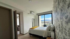 Un dormitorio con cama, una mesita de noche, una ventana con vistas y un equipo de aire acondicionado.