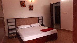 A bedroom with a wooden bed, white linens, a red blanket, and two wall-mounted paintings.