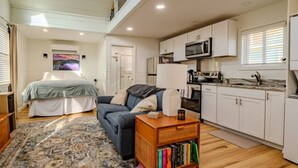 A compact living space with a sofa, a bookshelf, a dining area, and a kitchen. - Lake George Luxury Cabin (Alcove Studio) (Lake George)