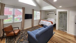 A room with a bed, a sofa, a chair, a TV, and a shower. - Lake George Luxury Cabin (Alcove Studio) (Lake George)