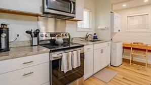 A compact kitchen with a microwave, stove, and oven, white cabinetry, and a wooden floor. - Lake George Luxury Cabin (Alcove Studio) (Lake George)