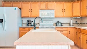Una cocina con armarios de madera, un refrigerador blanco, un microondas, una estufa y un lavabo.