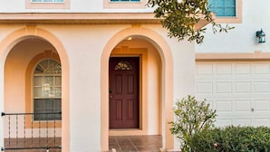 Una casa de dos pisos con puerta principal marrón, dos ventanas arqueadas y una puerta de garaje.