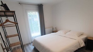 A bedroom with a bed, a wooden wardrobe, a radiator, and a window with curtains. - Separate F2 near RER&TGV and amenities (Massy)