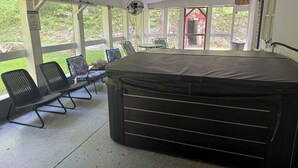 A covered outdoor area with a hot tub, chairs, and a table.