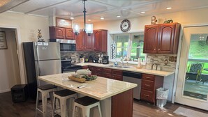 A modern kitchen with wooden cabinets, a central island with stools, a dishwasher, and a refrigerator.