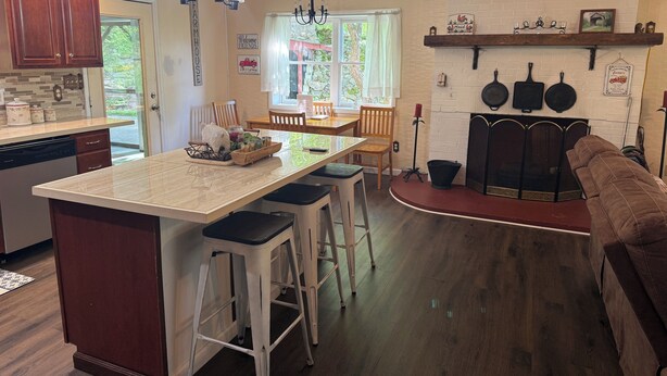 A kitchen with a central island, wooden bar stools, a fireplace, and a dining area with a window.