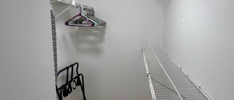 A small, enclosed storage area with a metal shelf, a hanging rack, and a carpeted floor.