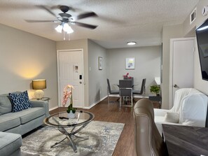 A modern living room with a sofa, coffee table, and a dining area with chairs and a table. - I207 - Apt|Patio|10mi to Convention Ctr|Sleeps 2 (Irving)