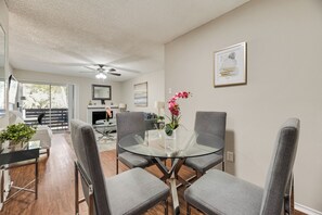 A modern dining area with a glass-top table, grey upholstered chairs, and a vase with pink flowers.