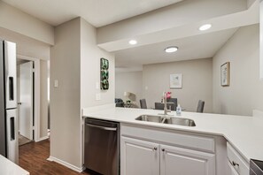 A modern kitchen with a built-in dishwasher, a stainless steel sink, and a dining area with a table and chairs.