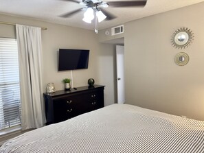 A bedroom with a bed, a dresser, a ceiling fan, a TV, and decorative wall mirrors.