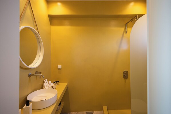 A bathroom with a round sink, a mirror, and a shower. - Niabelon Suites (Santorini)
