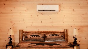 A wooden-paneled room with a bed, two bedside lamps, and an air conditioning unit on the wall. - Entire Cabin in Linn, MO with all the extras (Linn)
