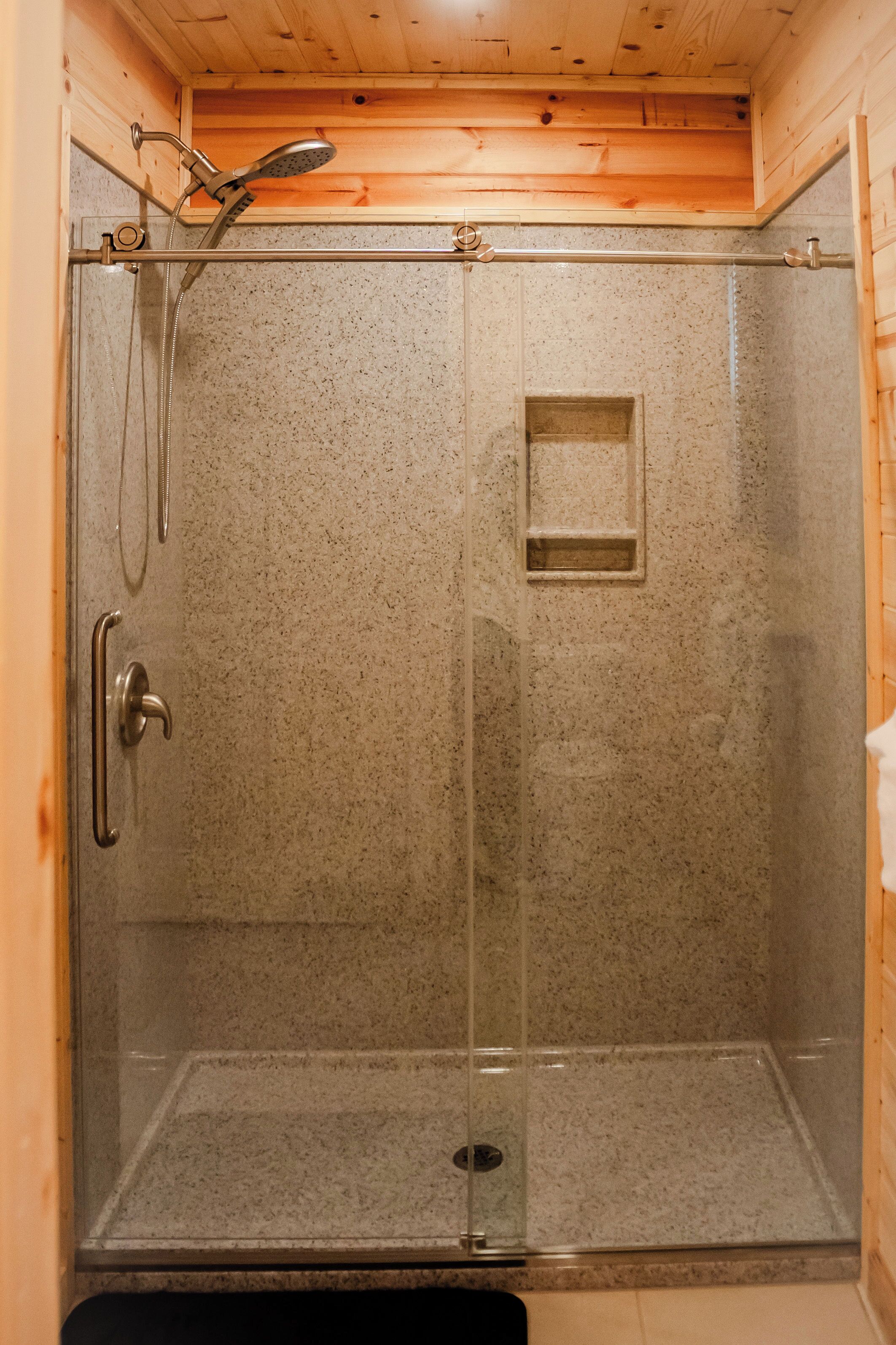 A glass-enclosed shower stall with a showerhead, a handrail, and a small shelf.