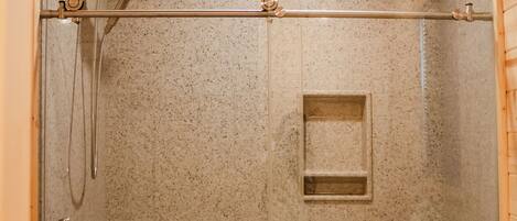 A glass-enclosed shower stall with a showerhead, a handrail, and a small shelf.