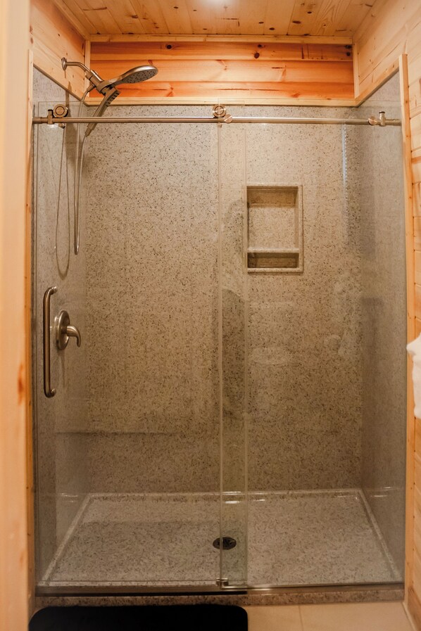 A glass-enclosed shower stall with a showerhead, a handrail, and a small shelf.