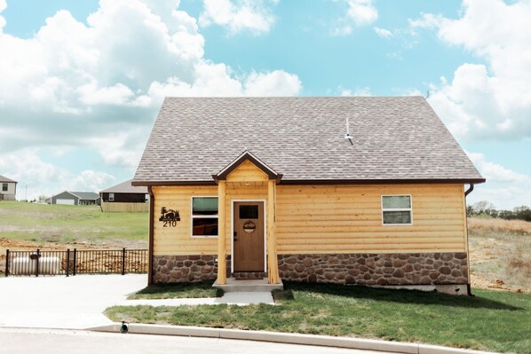 A single-story log cabin with a stone foundation, a gabled roof, and a small porch. - Entire Cabin in Linn, MO with all the extras (Linn)
