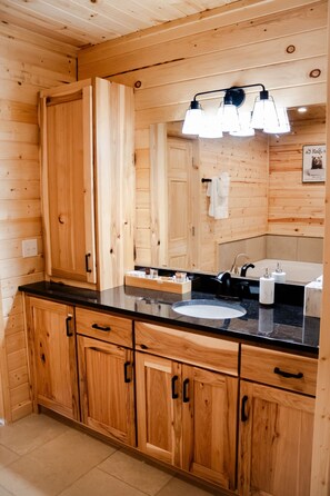A wooden cabin-style bathroom with a black countertop, a sink, and a mirror. - Entire Cabin in Linn, MO with all the extras (Linn)